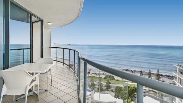 A balcony with a white table and chairs, overlooking a coastal view with the sea and a rocky shoreline. - Mantra Mooloolaba Beach (Mooloolaba)