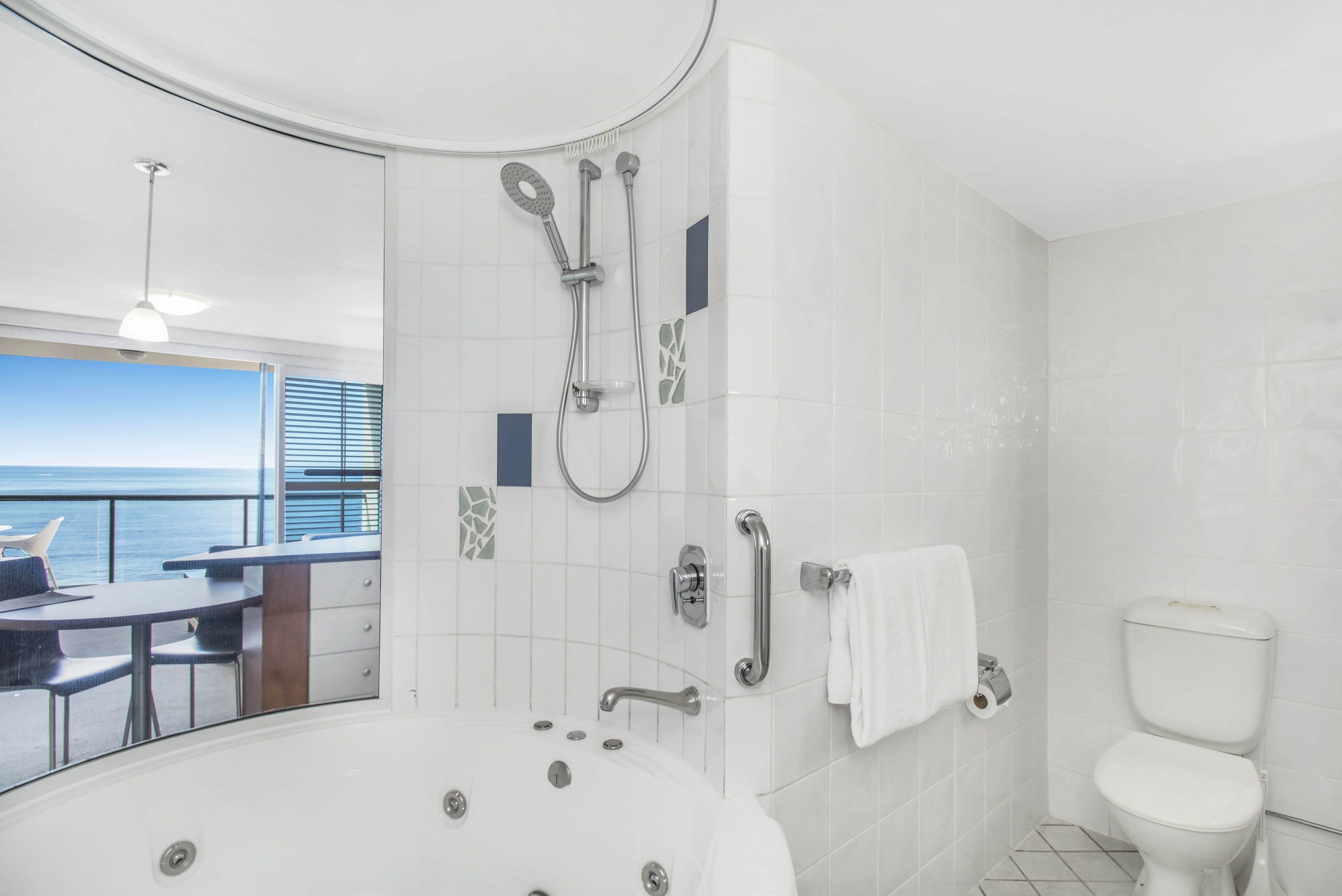 A modern bathroom with a bathtub, shower, toilet, and a window overlooking the sea.