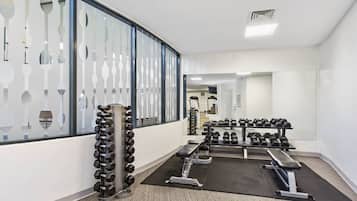 Een sportschool met trainingsapparatuur, waaronder gewichten en banken, en een groot raam met een decoratief patroon.