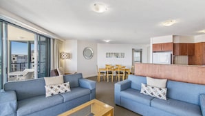A modern living room with two sofas, a coffee table, and a dining area with chairs and a table. - Mantra Mooloolaba Beach (Mooloolaba)