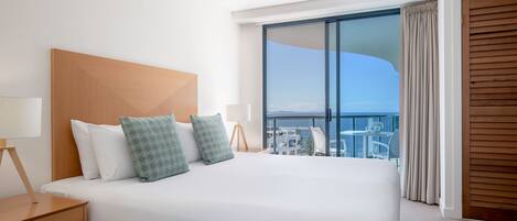 A hotel room with a large bed, a nightstand, a lamp, and a view of the balcony and outside scenery.