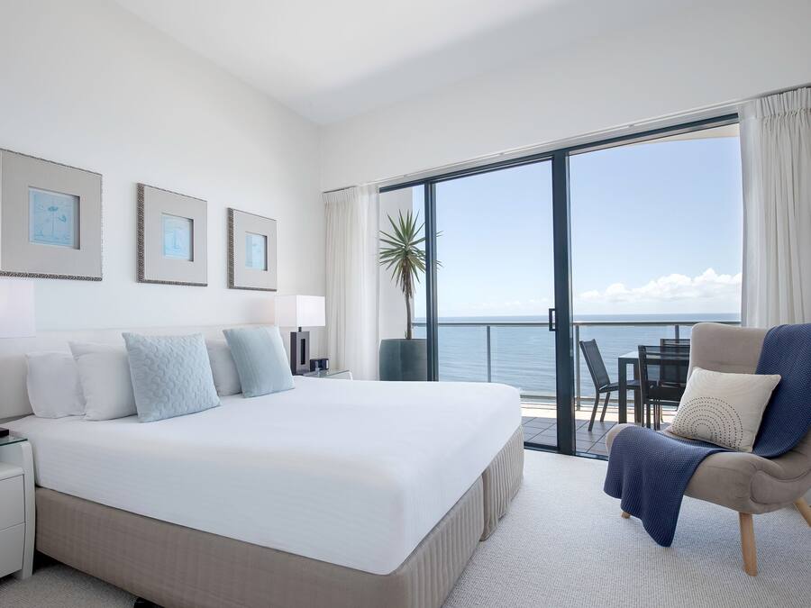 Camera d'hotel moderna con un letto grande, un angolo salotto con una poltrona e un balcone vista mare.