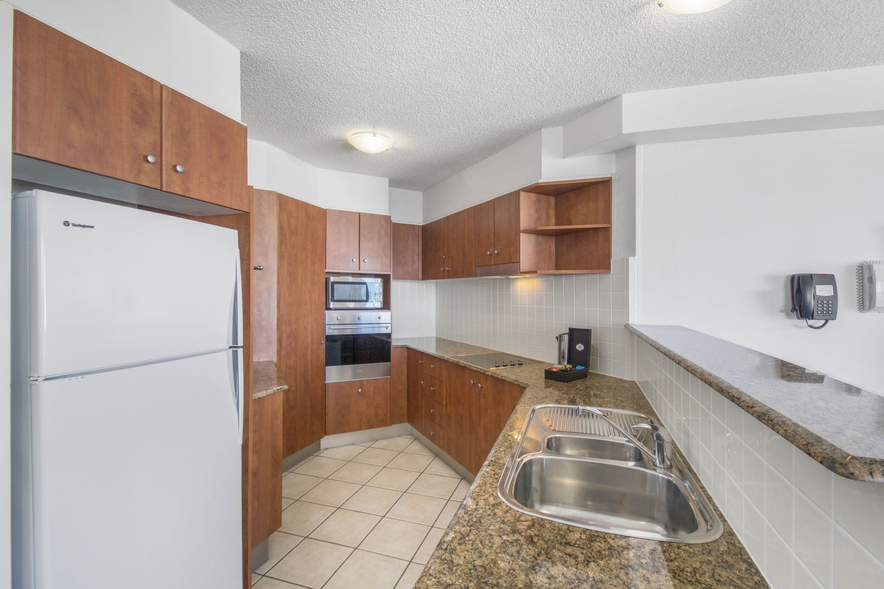 A kitchen with wooden cabinets, a stainless steel sink, a refrigerator, and a microwave.