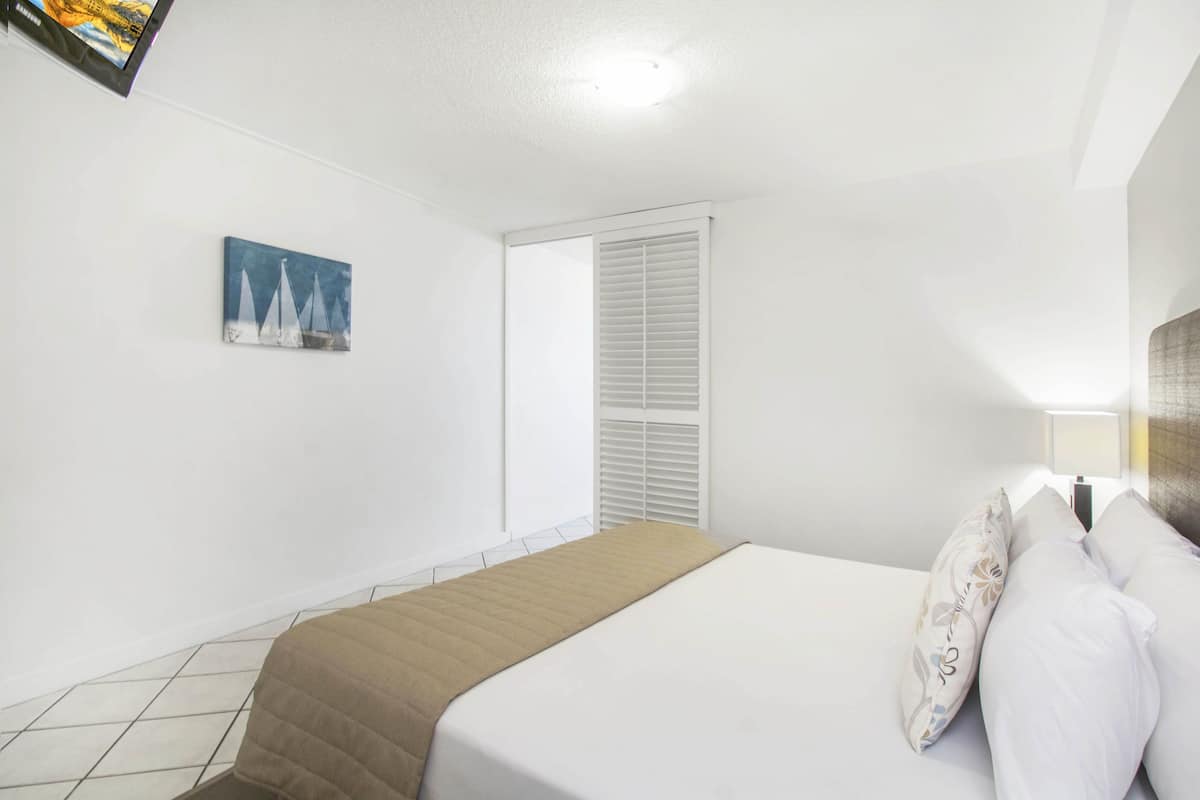 Un dormitorio con una cama, una ventana con persianas, un cuadro en la pared y suelo de baldosas.