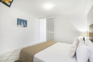 Un dormitorio con una cama, una ventana con persianas, un cuadro en la pared y suelo de baldosas.