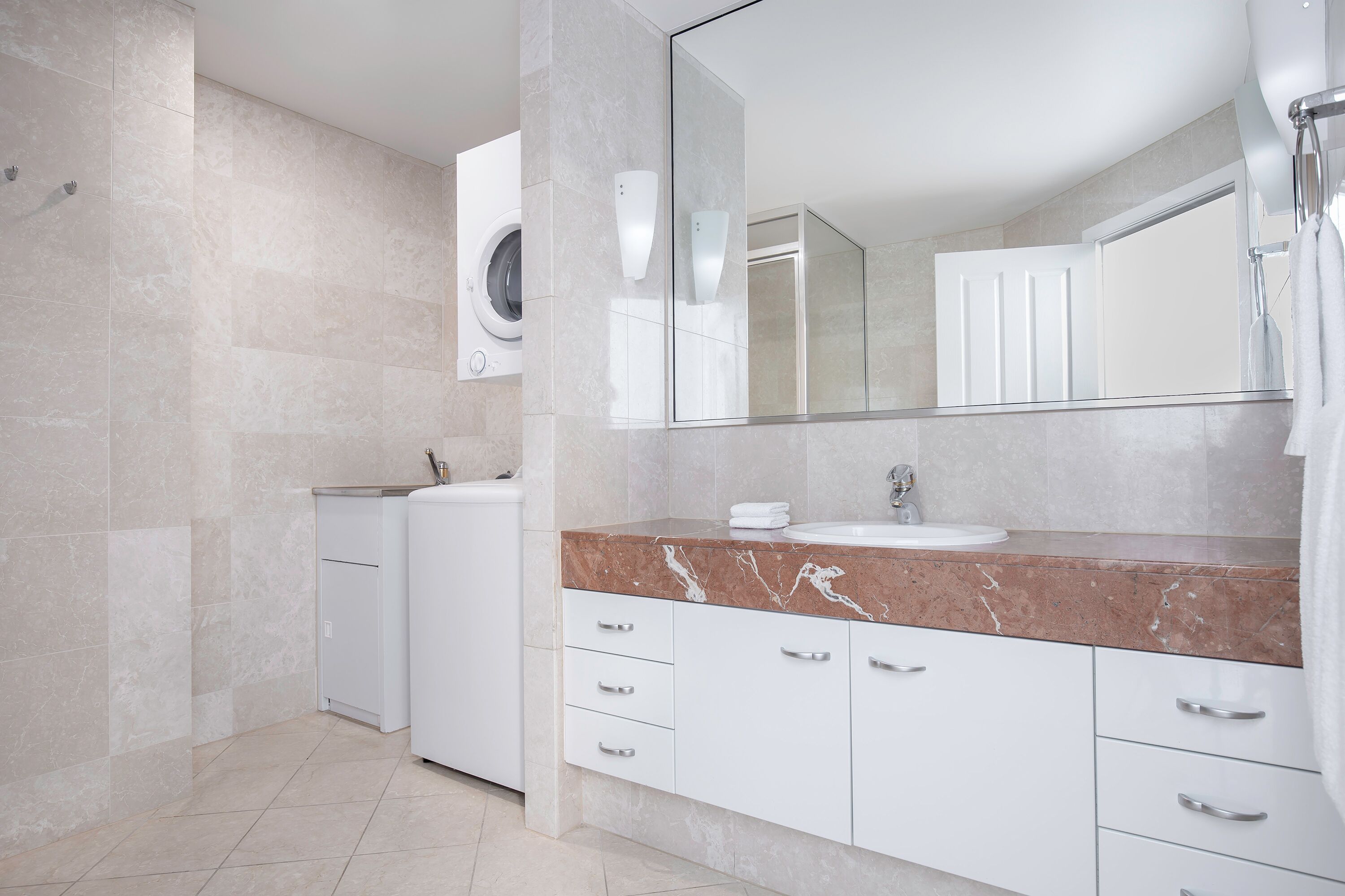 A modern bathroom with a marble countertop, a large mirror, a sink, and a built-in washing machine.
