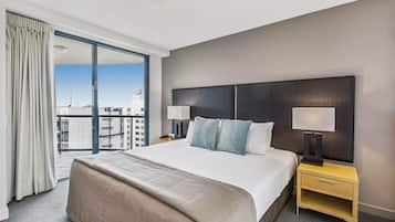 A hotel room with a large bed, two bedside lamps, a nightstand, and a view of the city through a large window.
