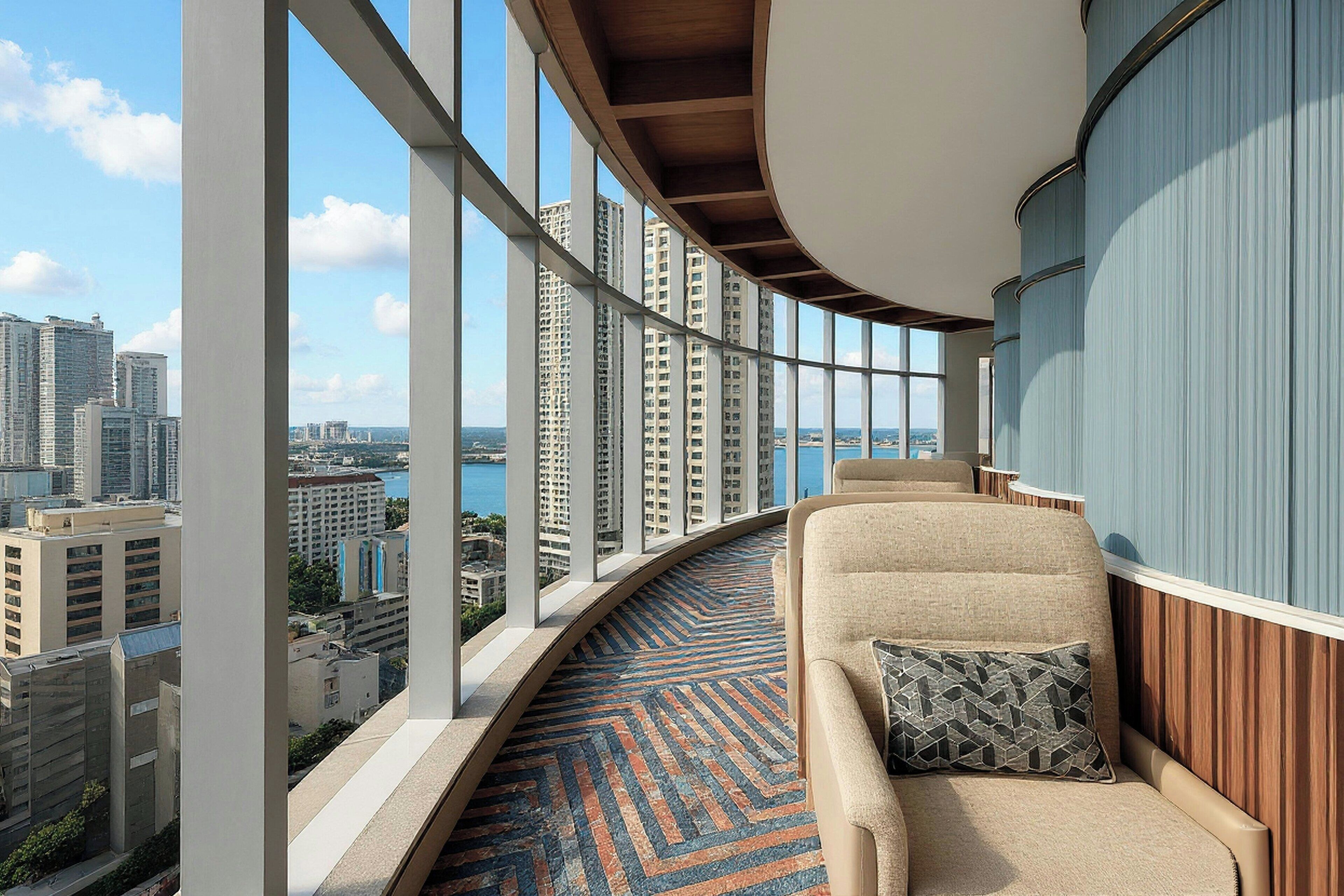 A balcony with a curved railing, a sofa with a patterned cushion, and a view of a cityscape with high-rise buildings.