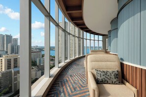 Un balcón con barandilla curva, un sofá con cojín estampado y vistas a un paisaje urbano con edificios altos.
