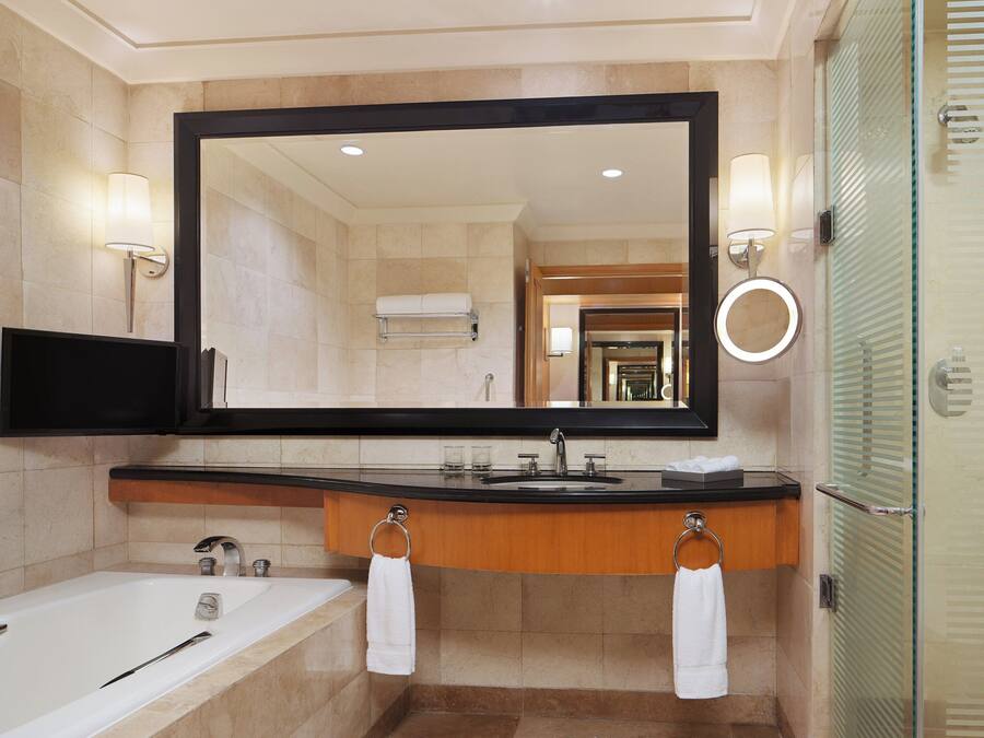 A modern bathroom with a large mirror, a bathtub, a sink, and a glass shower enclosure.