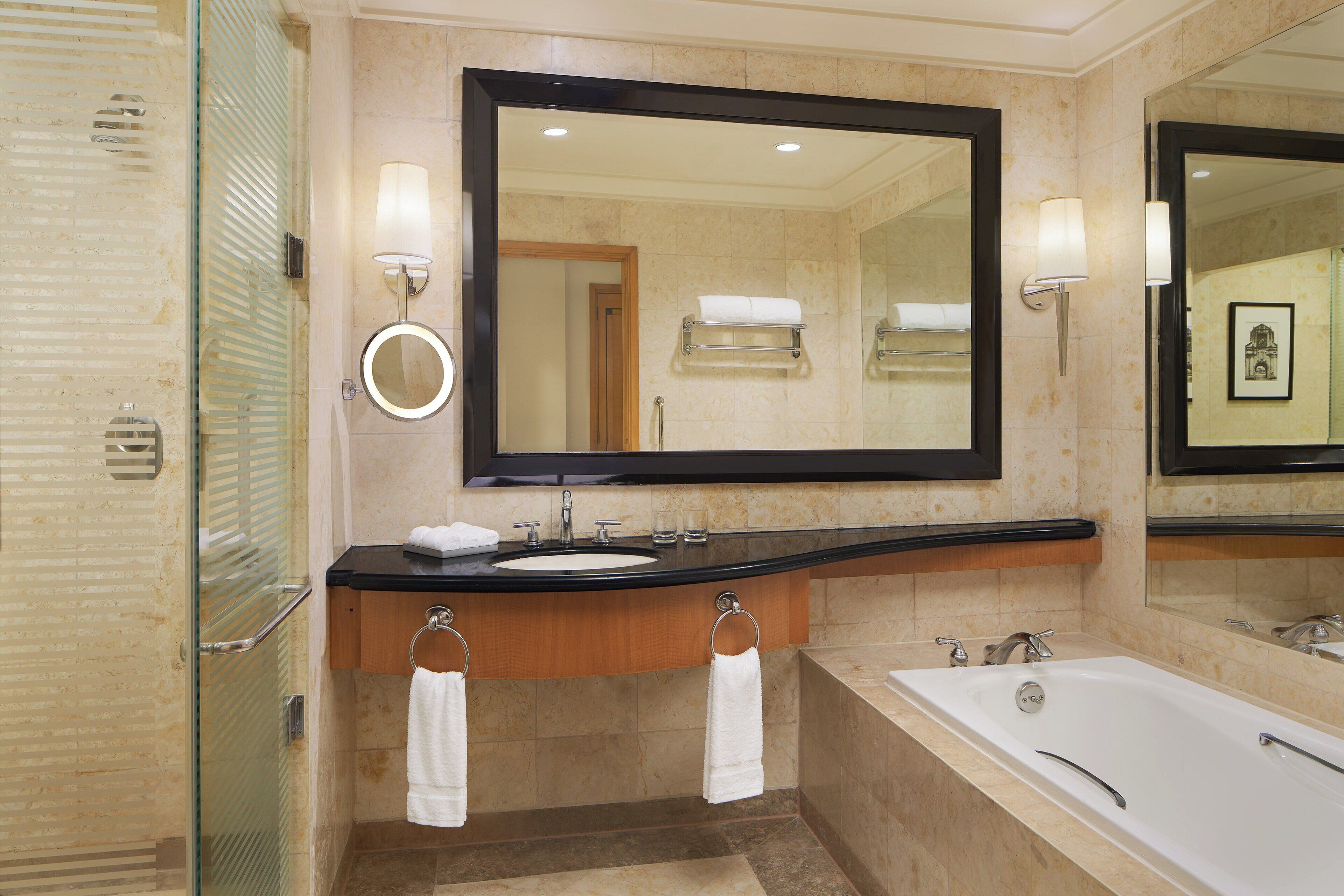 A modern bathroom with a large mirror, two sinks, a bathtub, and a glass-enclosed shower.