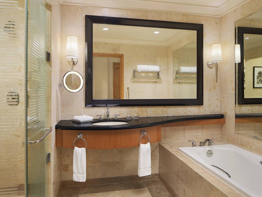 A modern bathroom with a large mirror, two sinks, a bathtub, and a glass-enclosed shower.