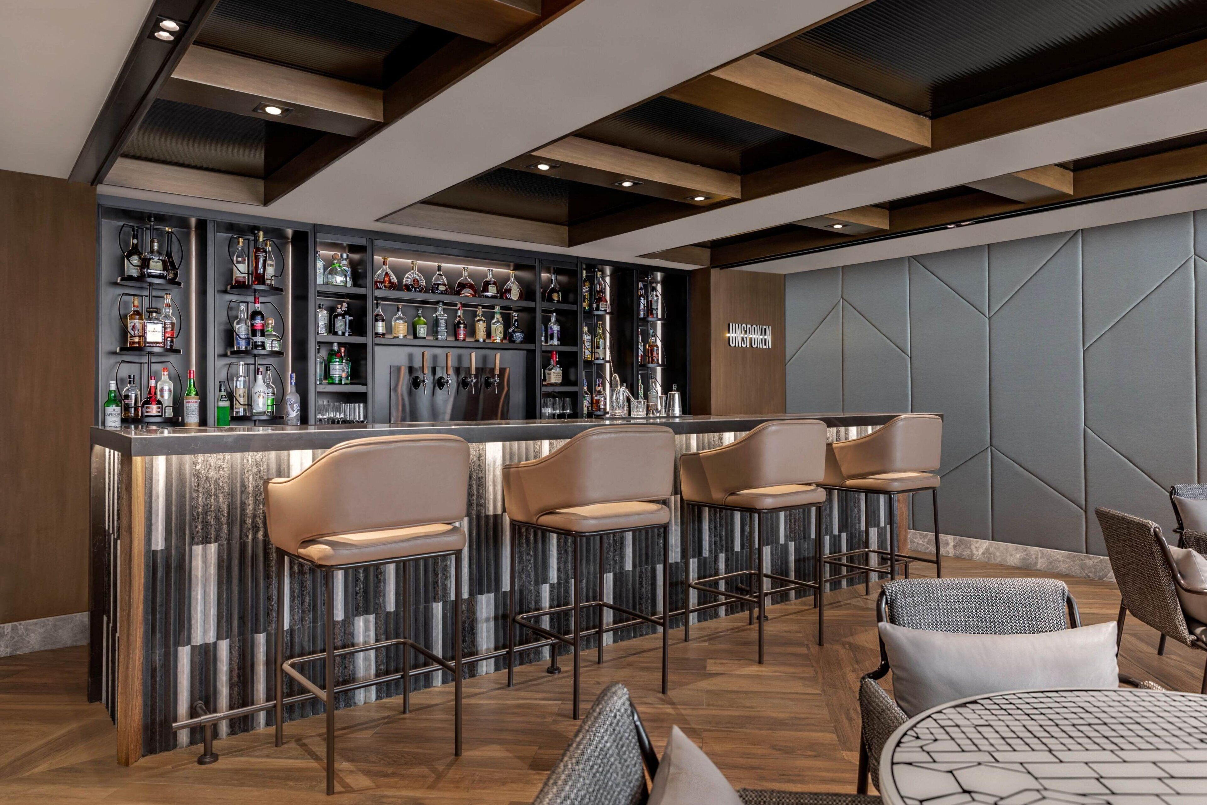Un espace bar doté d’un comptoir en marbre, de nombreuses bouteilles d’alcool et de tabourets de bar.