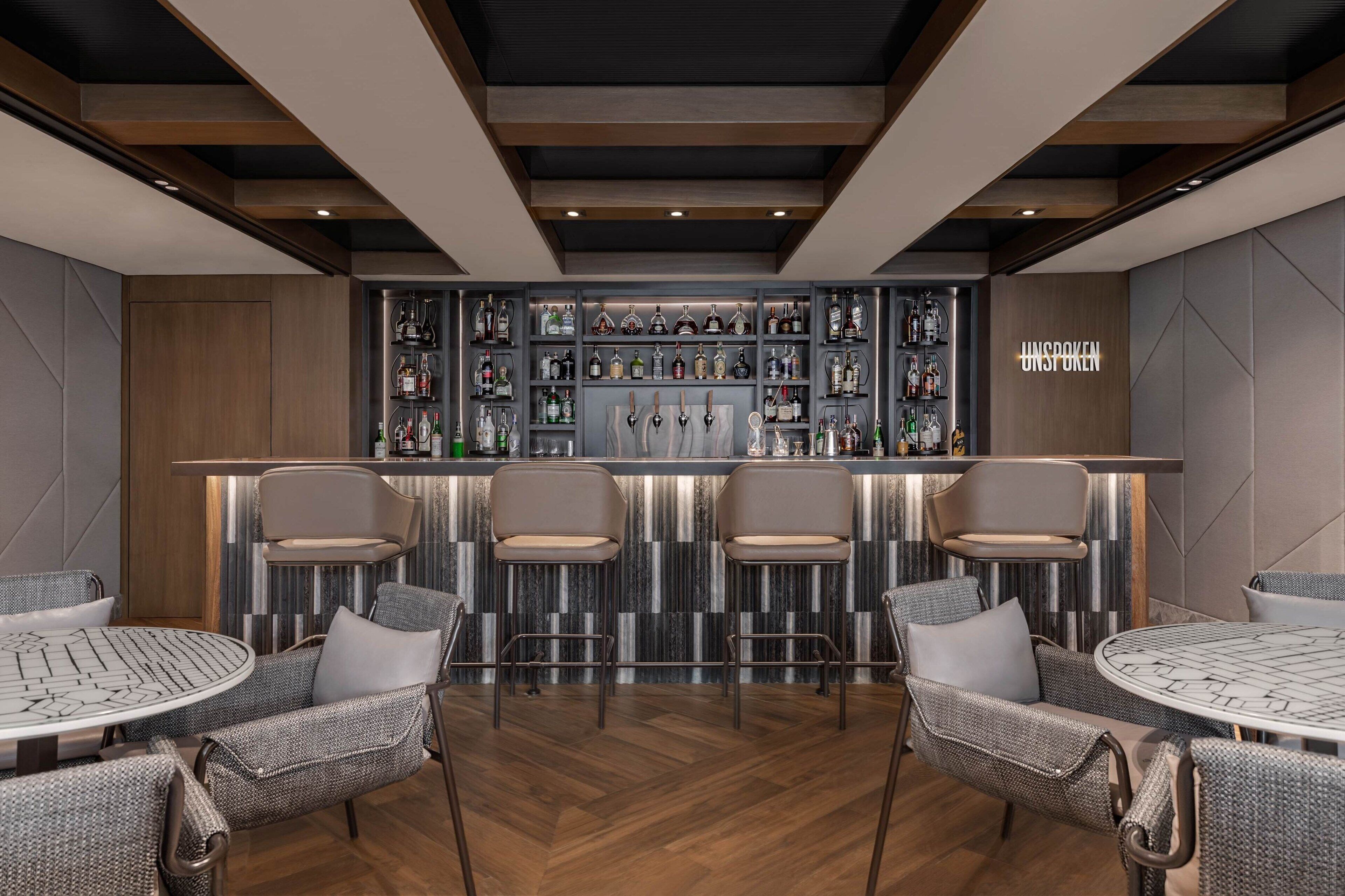 A bar area with a modern design, featuring a bar counter, multiple seating options, and a variety of bottles displayed on shelves.