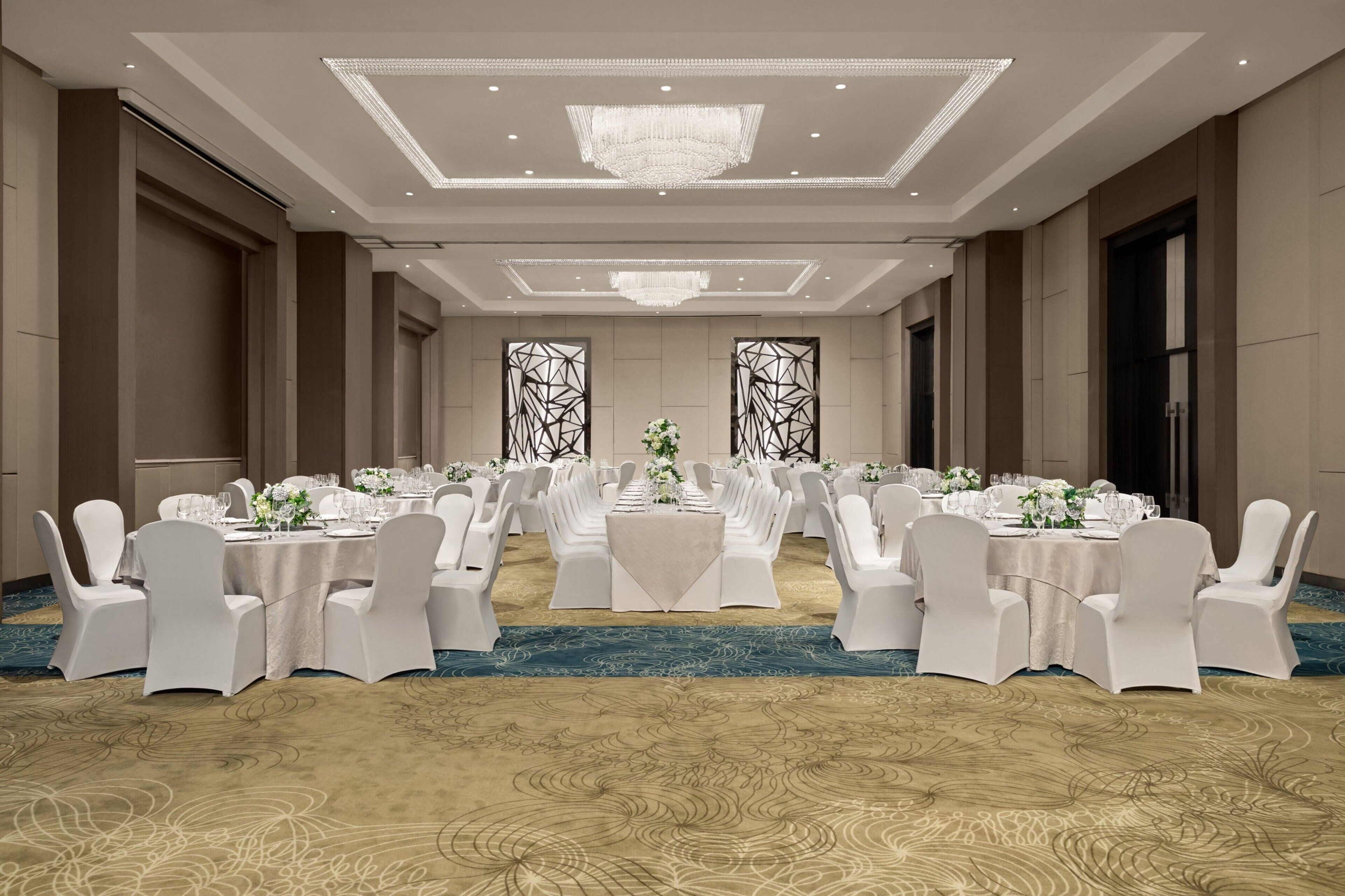 A banquet hall with round tables, white chairs, and chandeliers.