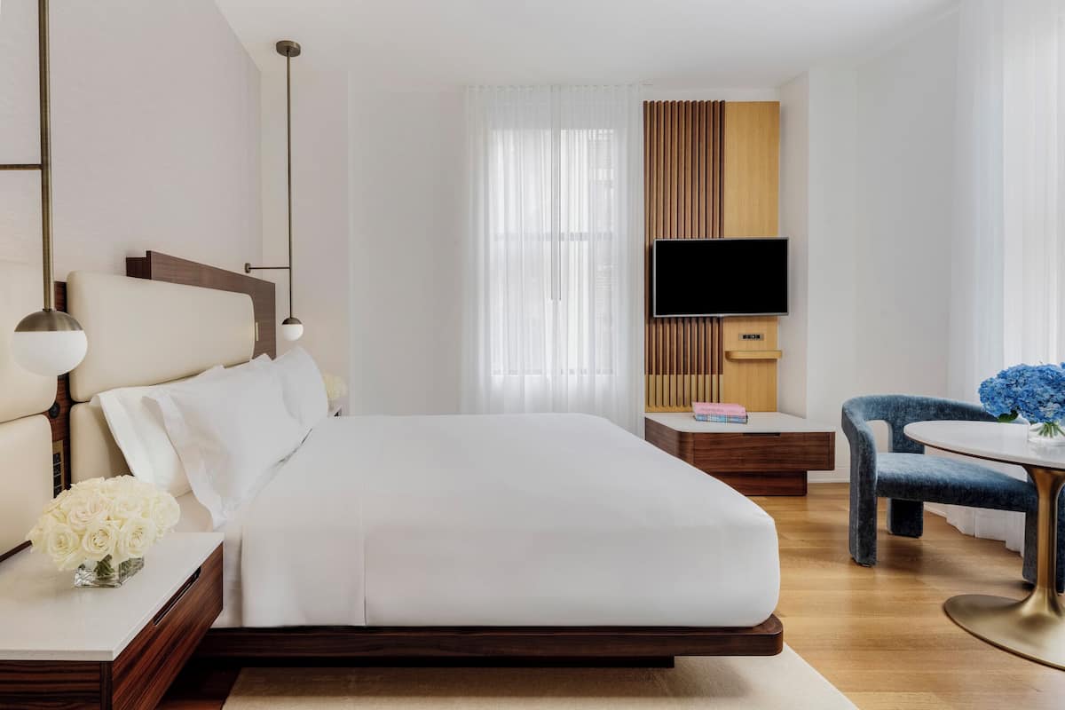 Egy modern szállodai szoba, amelyben egy nagy ágy, egy íróasztal, egy szék, egy televízió és egy ablak található, melyen könnyű, áttetsző függöny van.