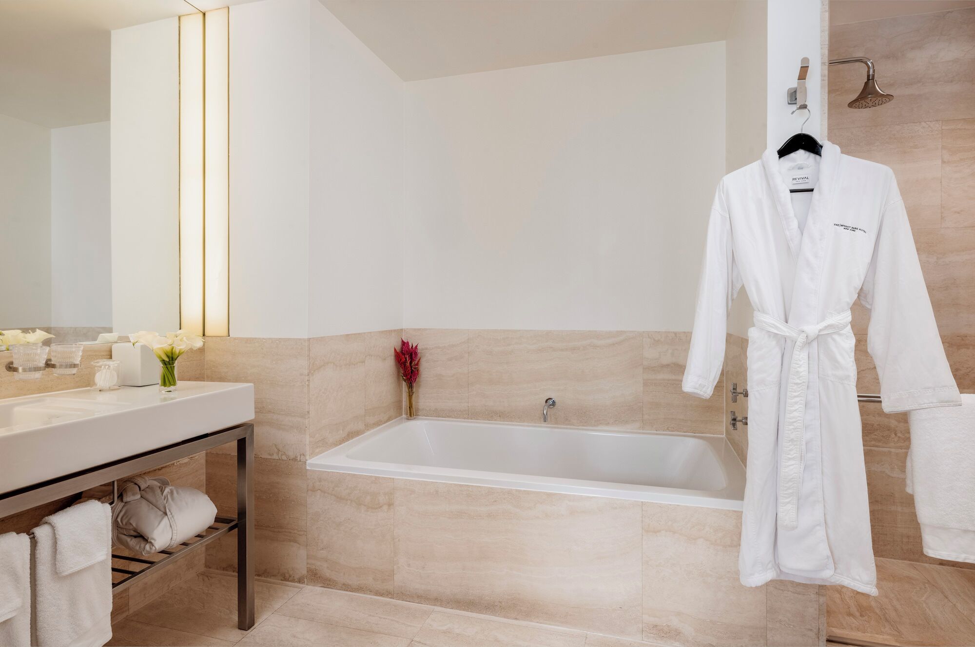 Ein modernes Badezimmer mit Badewanne, Waschtisch und Spiegel sowie einem auf einem Koffergestell hängenden Bademantel.