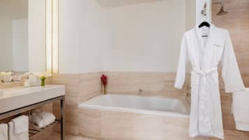 Ein modernes Badezimmer mit Badewanne, Waschtisch und Spiegel sowie einem auf einem Koffergestell hängenden Bademantel.