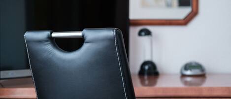 Una silla de cuero negro con estructura metálica, un escritorio de madera, una lámpara negra y un cuadro en la pared.
