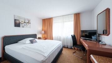 Habitación de hotel con cama, escritorio con televisor, silla, lámpara y un cuadro en la pared.