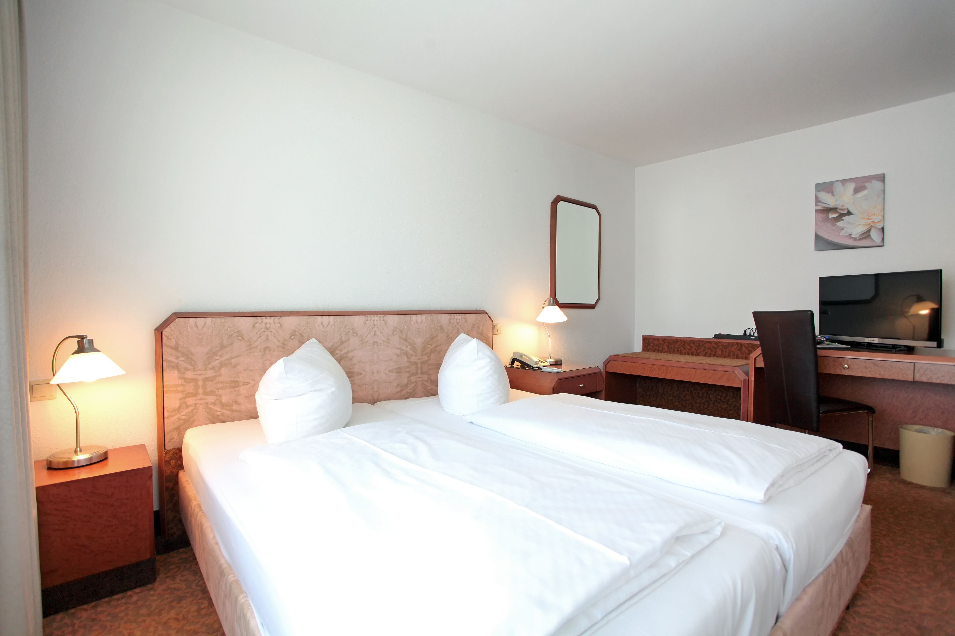 A hotel room with a large bed, a desk with a computer, a TV, and two bedside lamps.