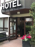 A hotel entrance with a large sign, a bench, and potted plants.