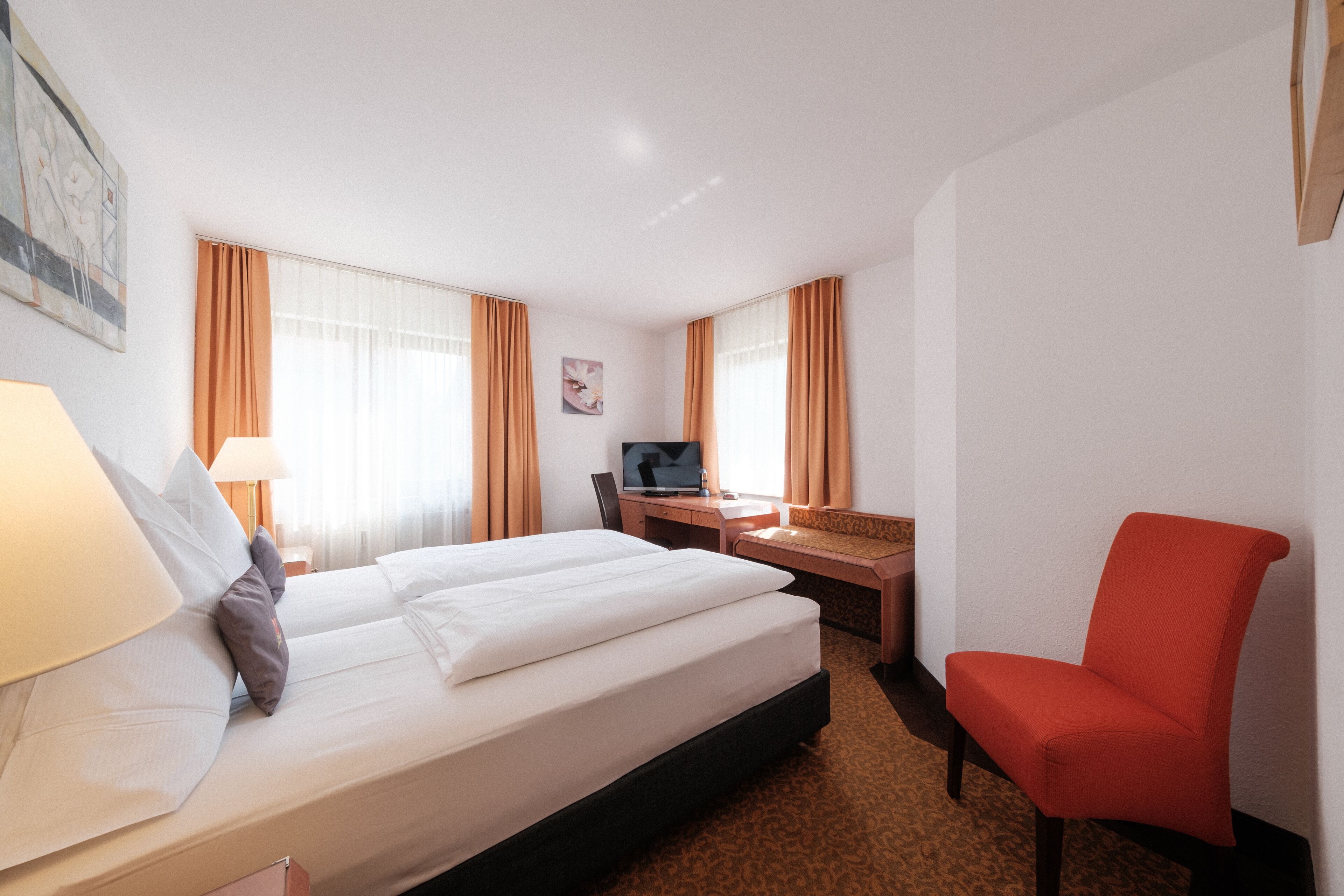 A hotel room with a bed, desk, chair, and a TV.