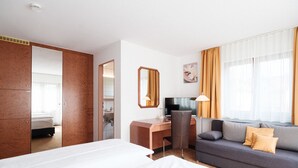 A hotel room with a bed, a desk, a chair, a sofa, and a large window with curtains. - Hotel Flora Stuttgart - Möhringen (Stuttgart)