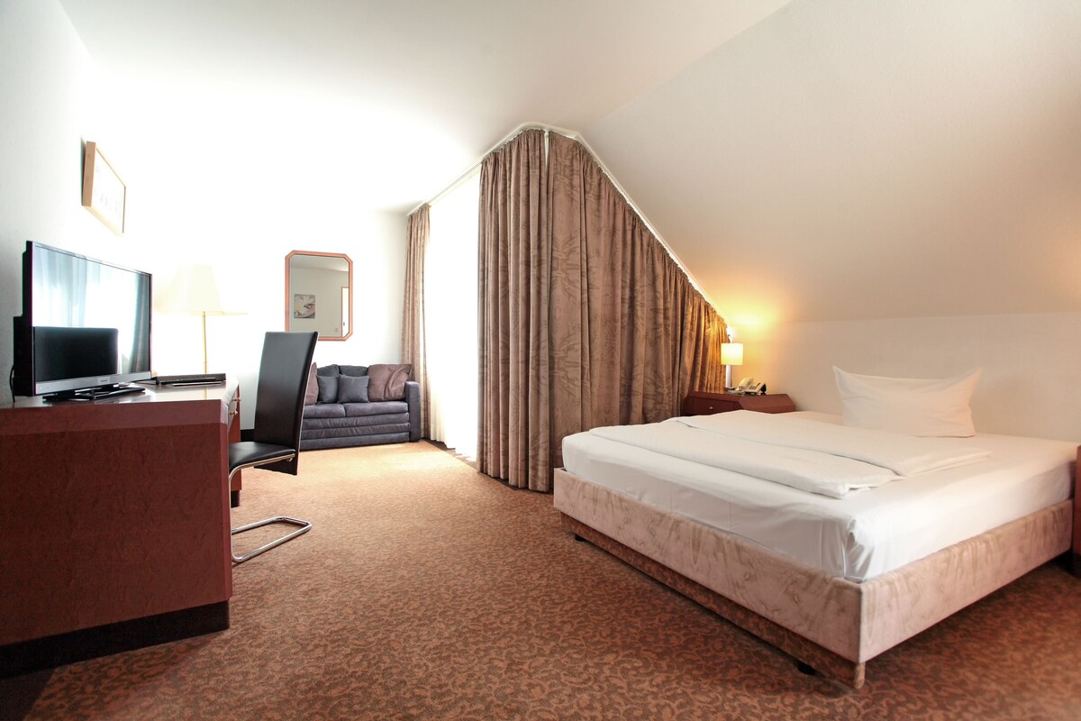A hotel room with a bed, a desk, a chair, a television, a lamp, and a mirror.