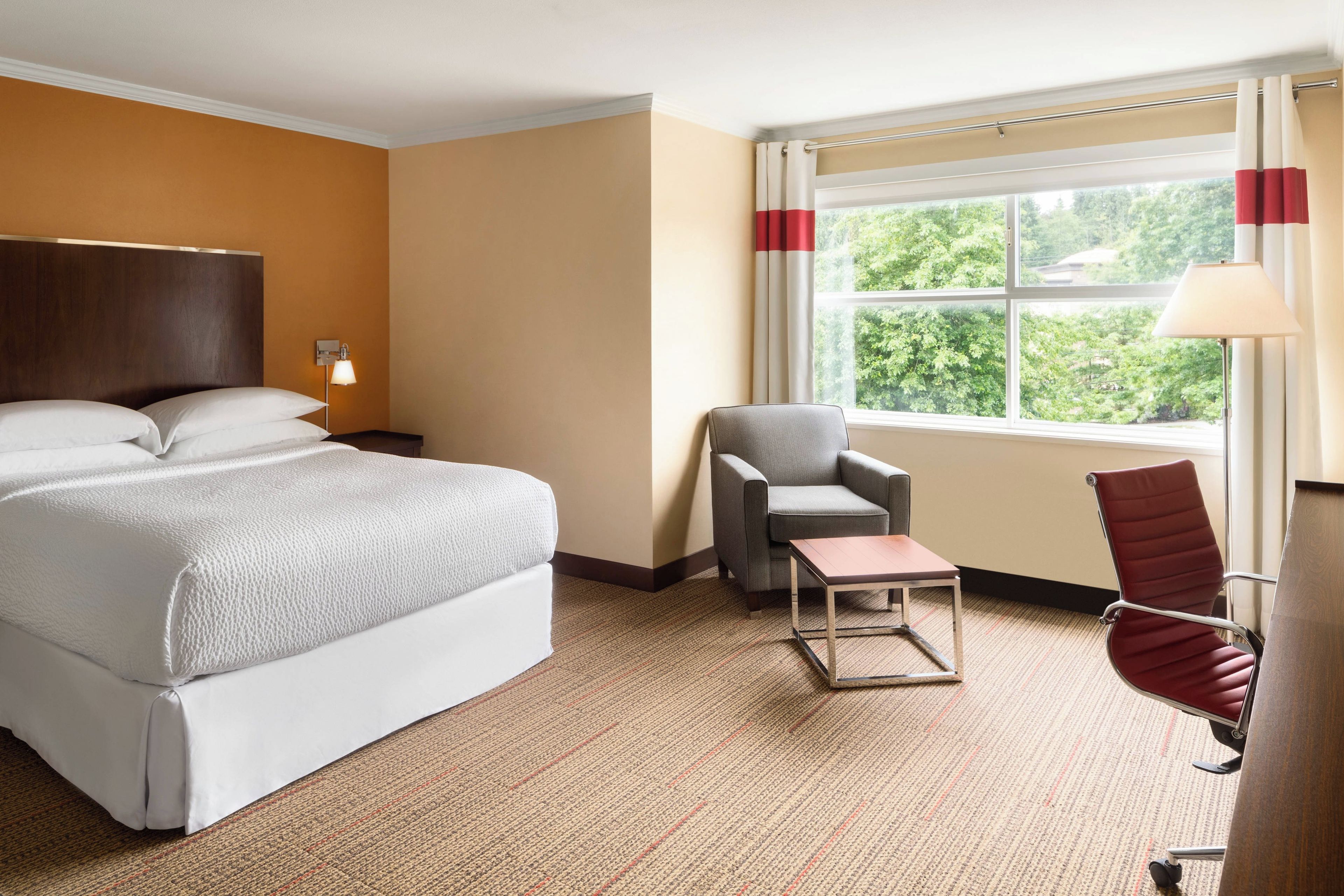 Una habitación de hotel con cama, escritorio, silla y ventana con cortinas.
