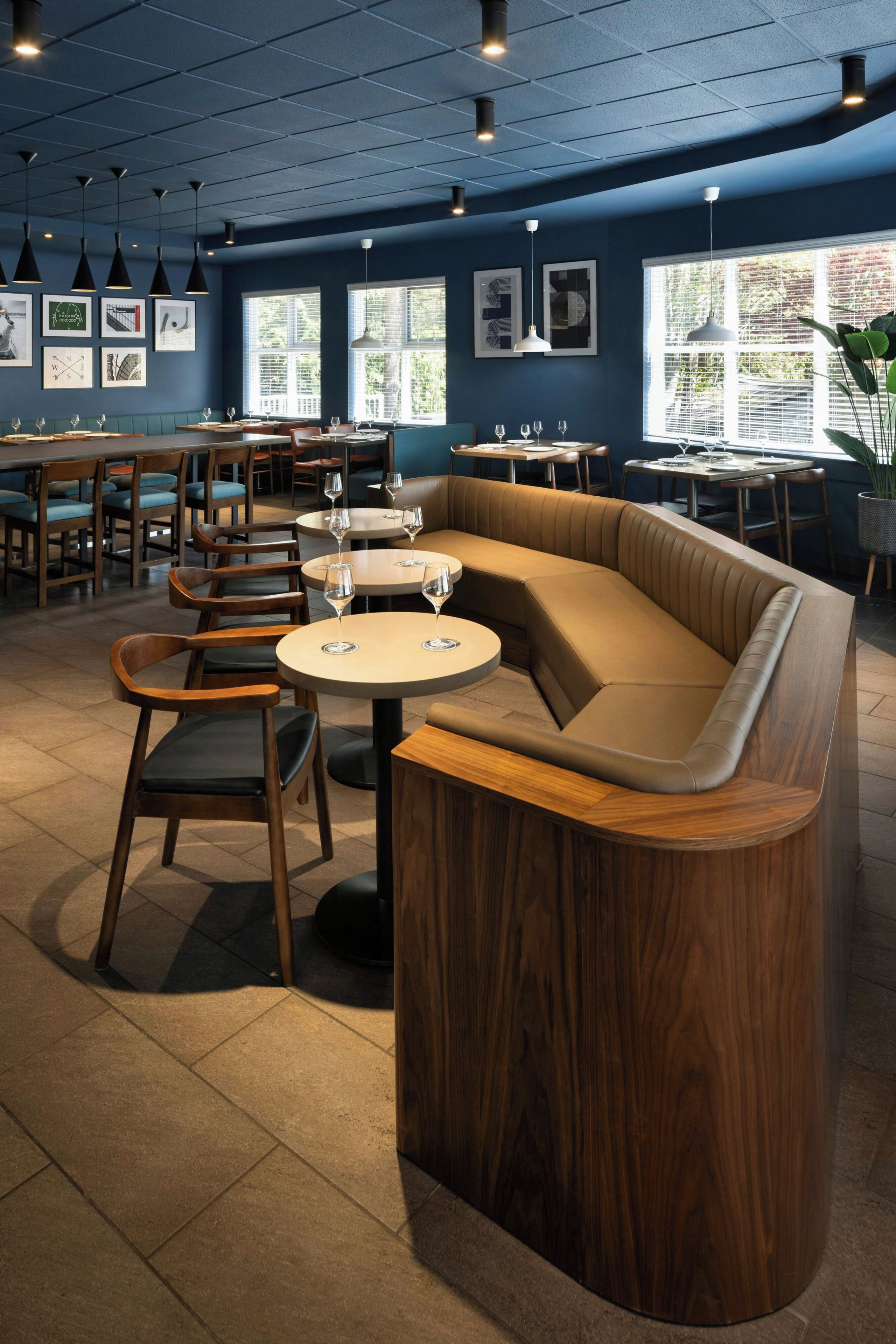 Un interior de restaurante moderno con una zona central de asientos que incluye un banco de madera y mesas redondas, rodeadas de sillas.