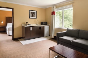 Una habitación de hotel con kitchenette, un sofá, una mesa de centro y una cama.