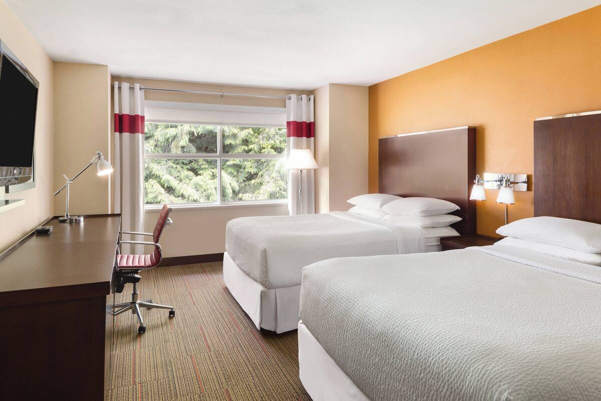 Habitación de hotel con dos camas, un escritorio con silla, televisor y ventana con cortinas.