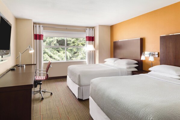 Habitación de hotel con dos camas, un escritorio con silla, televisor y ventana con cortinas.