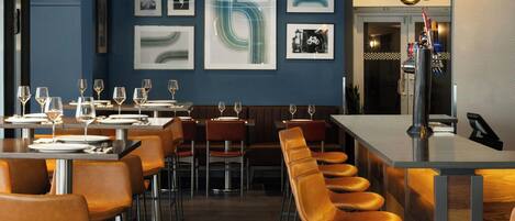 A modern bar area with high stools and a long counter, featuring a mix of framed artwork and a bicycle-themed picture.