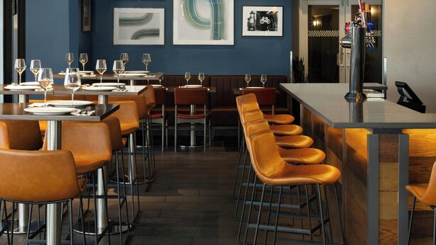 A modern bar area with high stools, a long counter, and a ceiling with exposed beams. - Four Points by Sheraton Surrey (Surrey)