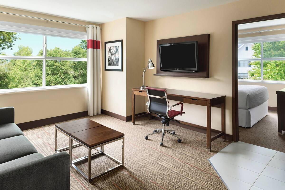 Una habitación de hotel con un ventanal grande, un escritorio con silla, un televisor y un sofá.