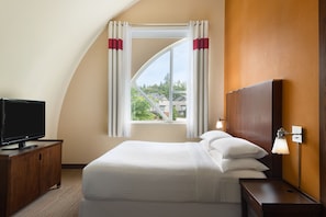 A hotel room with a bed, a TV on a wooden cabinet, a window with curtains, and a nightstand with a lamp. - Four Points by Sheraton Surrey (Surrey)