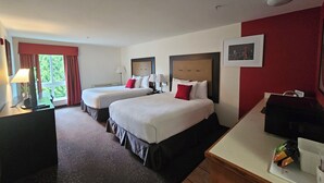 A hotel room with two beds, a desk, a coffee machine, and a window with curtains.
