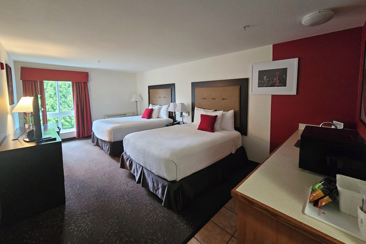 A hotel room with two beds, a desk, a coffee machine, and a window with curtains.
