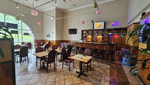 A restaurant with a bar area, tables, chairs, and a large window.