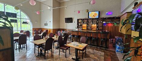 A restaurant with a bar area, tables, chairs, and a large window.