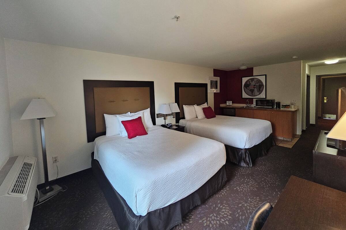 A hotel room with two beds, a desk, a microwave, and a small kitchenette.