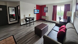 A modern hotel room with a dining area, a sofa, a TV, and a window with curtains.