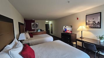 A hotel room with two beds, a desk, a television, and a cityscape painting.