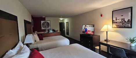 A hotel room with two beds, a desk, a television, and a cityscape painting.
