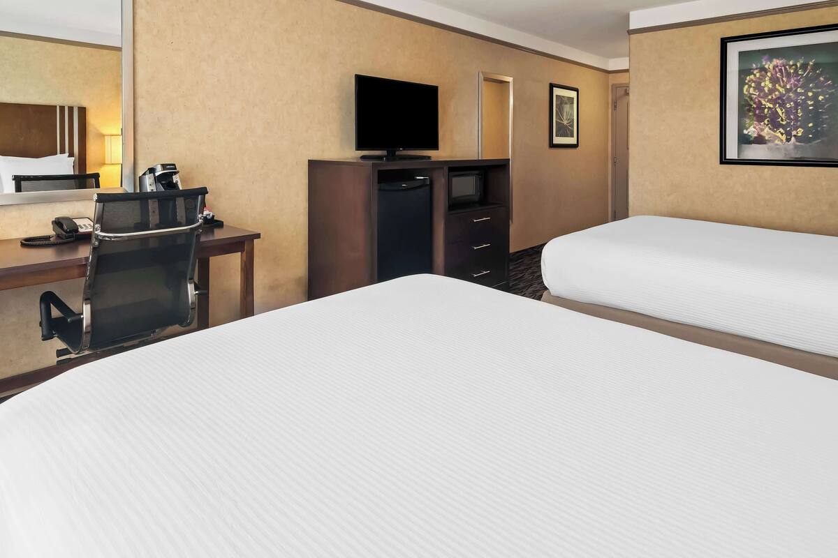 A hotel room with a large bed, a desk with a telephone, a coffee maker, a television, and a mirror.