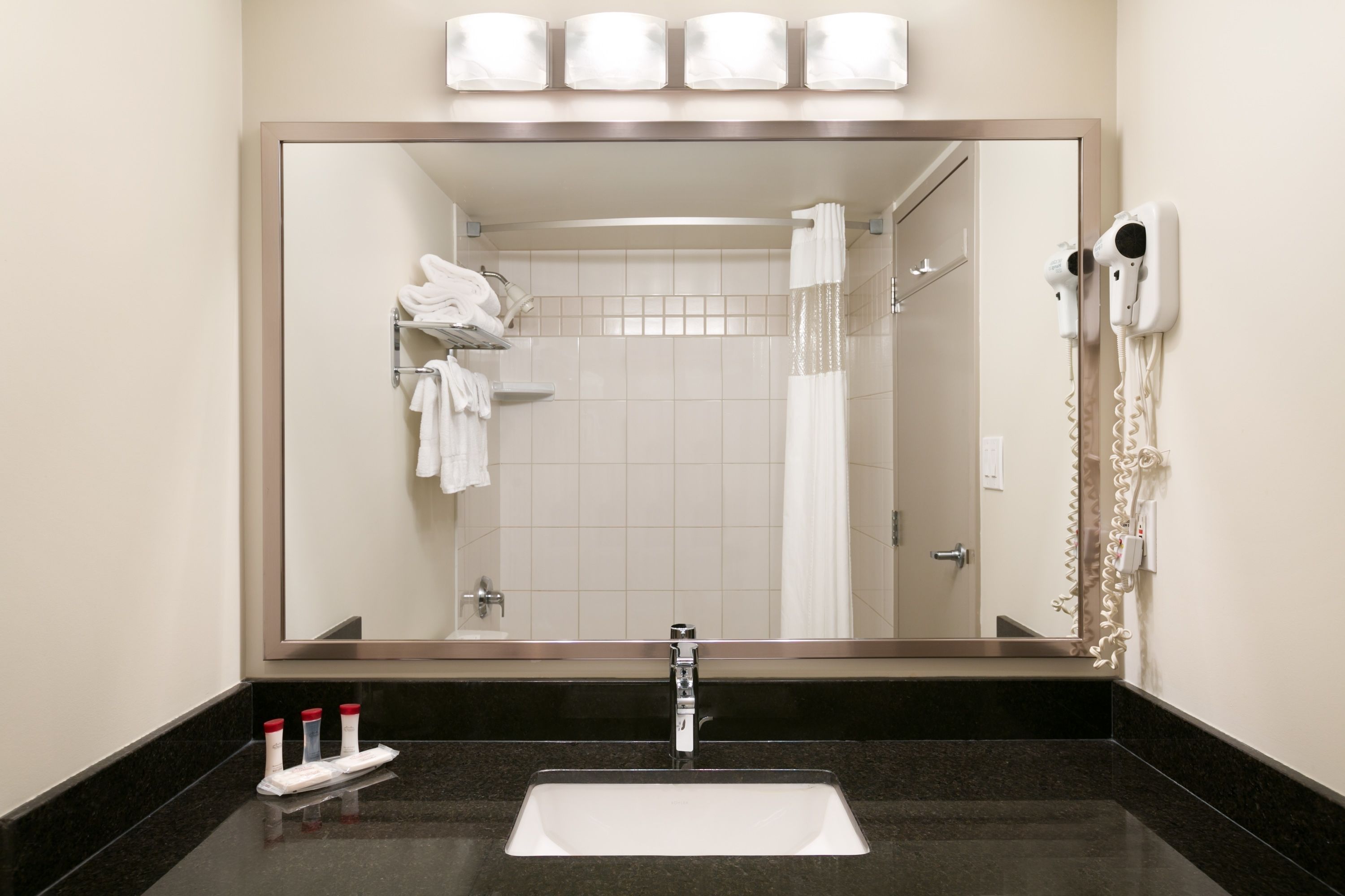 A bathroom with a large mirror, a sink, a towel rack, and a hairdryer.