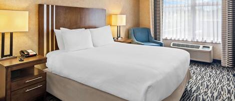 Habitación de hotel con una cama grande, dos mesitas de noche con lámparas, una silla y una ventana con cortinas.