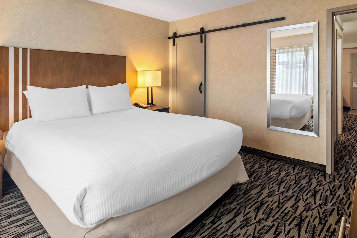 A hotel room with a large bed, a nightstand with a lamp, a sliding door, and a mirror.